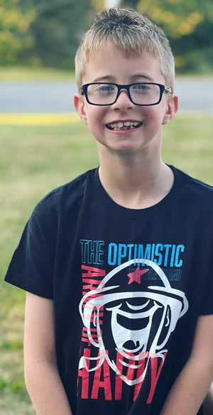 Child wearing black t-shirts with graphics and text, standing outdoors.
