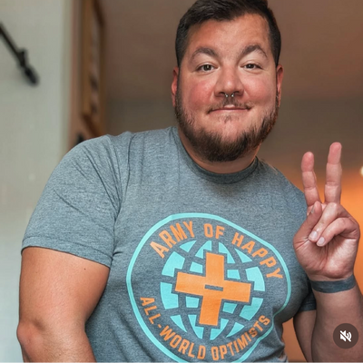 Man wearing a gray t-shirt with a logo and text, making a peace sign.