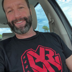 Man wearing a black Army of Happy t-shirt with a red logo inside a car